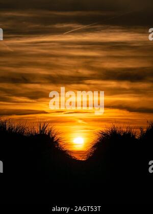 Cielo drammatico con il sole che tramonta dietro marram erba dune coperte in primo piano Foto Stock