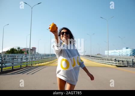 una ragazza in una felpa con cappuccio sportiva lancia un arancio come un baseball. sport, fitness Foto Stock