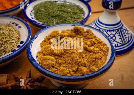 Cibo sano. Le spezie in contenitori in ceramica tipica del Marocco su un vecchio tavolo di legno. Curcuma, cumino, anice stellato, aneto e timo Foto Stock