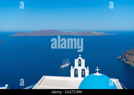 Tre campane di Fira, ufficialmente la Chiesa cattolica di Koimisi Tis Theotokou, una chiesa greco-cattolica di Santorini con la vela nave da crociera in blu Foto Stock