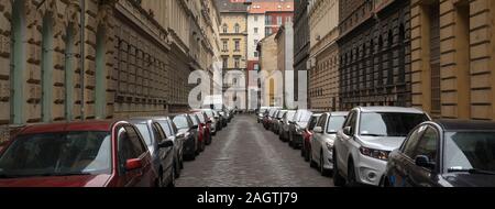 Molte automobili parcheggiate in linea su entrambi i lati della vecchia città europea street Foto Stock