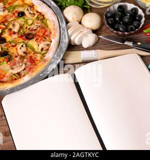 Pane appena sfornato la pizza con il vuoto o notebook cookbook circondato da vari ingredienti. Foto Stock