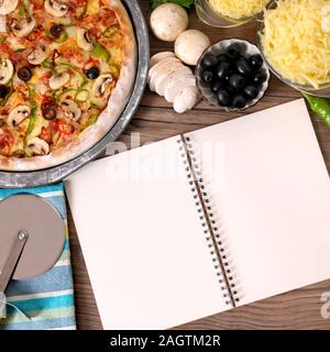 Pane appena sfornato la pizza con il vuoto o notebook cookbook circondato da vari ingredienti. Foto Stock