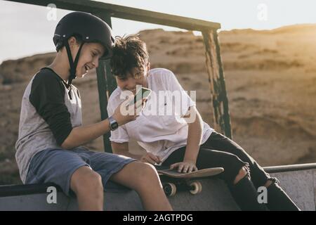 Coppia di amici gustando il tempo libero al skatepark guardando il video di halfpipe trucchi online. Gli adolescenti divertirsi con lo skateboard la condivisione dei file multimediali Foto Stock