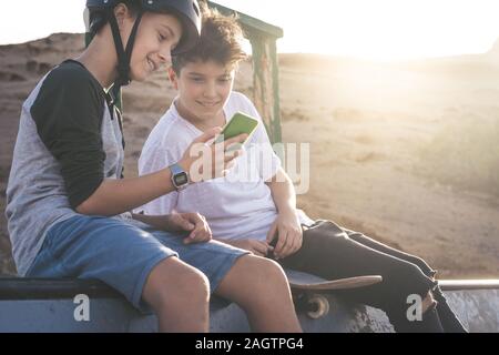 Due giovani boy utilizza lo smartphone a skate park, seduto su un halfpipe ramp. I ragazzi di comunicare con gli amici con un telefono cellulare la condivisione di video da s Foto Stock