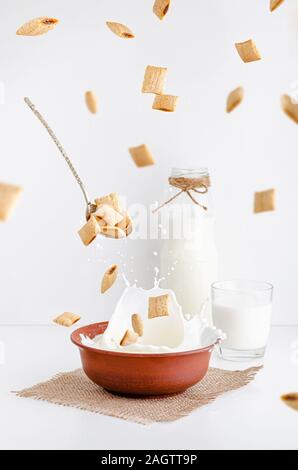 La prima colazione a secco di cereali piazzole di mais con ripieno di cacao in argilla rossa ciotola con latte da agricoltura biologica. Levitazione e battenti concetto alimentare. Foto Stock