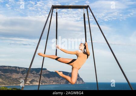 Donna pratica fly dance gravità lo yoga pone in una amaca all'aperto con vista montagna. Uno stile di vita sano, attivo della donna. Foto Stock