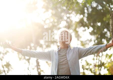 Senior uomo asiatico godendo di aria fresca passeggiando con le braccia aperte all'esterno in posizione di parcheggio Foto Stock
