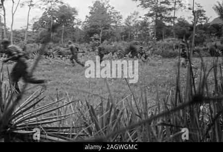 Soldati olandesi attraversano un campo aperto con armi presso il pronto in Indonesia, Indie olandesi, Sumatra ca. Dicembre 25, 1948 Foto Stock