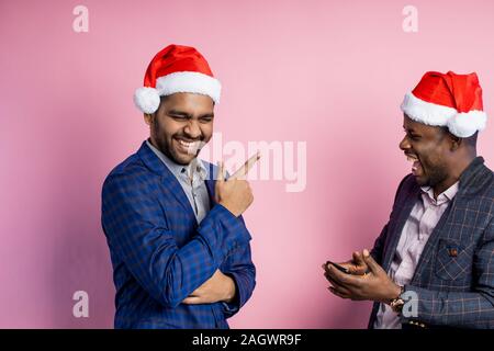 Due contentissimo amici maschi allegramente parlando, ridevano forte, indicando le dita in ogni altra, in piedi su sfondo rosa. Indiani e Africani l'uomo Foto Stock