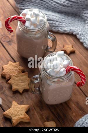 Due tazze di vetro con il cacao, marshmallows, lo zucchero di canna e lo zenzero i cookie su un sfondo di legno. Orientamento verticale Foto Stock