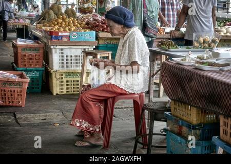 Anziani Thailandia donna seduta su uno sgabello e mangiare in un mercato tailandese Foto Stock