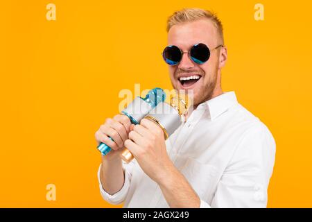 Bellissimo uomo caucasico con gli occhiali canta canzoni karaoke con microfono isolato su sfondo giallo Foto Stock