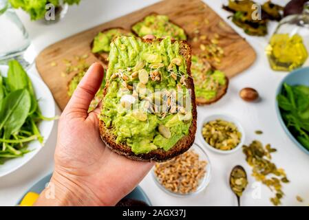 Guacamole Avocado Sandwich in una femmina di mano con i semi di zucca e piantine di frumento Foto Stock