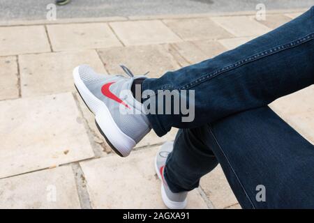 Athens, Grecia - 30 Novembre 2019: Uomo seduto in sneakers grigio e blu scuro jeans con logo rosso Foto Stock