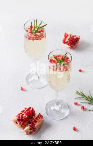 Due bicchiere di melagrana vacanze di Natale cocktail con il rametto di rosmarino, vino frizzante, club soda sul tavolo bianco. Xmas drink. Close up. Foto Stock