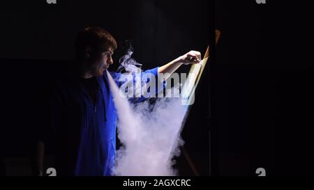 Artista copista paint seascape con nave in oceano. Fumo Vaper vape e-sigaretta. Artigiano arredatore disegnare come barca vela sul mare blu con colori acrilici. Foto Stock