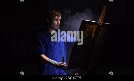 Artista copista paint seascape con nave in oceano. Fumo Vaper vape e-sigaretta. Artigiano arredatore disegnare come barca vela sul mare blu con colori acrilici. Foto Stock