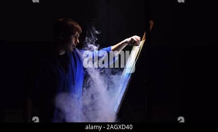 Artista copista paint seascape con nave in oceano. Fumo Vaper vape e-sigaretta. Artigiano arredatore disegnare come barca vela sul mare blu con colori acrilici. Foto Stock