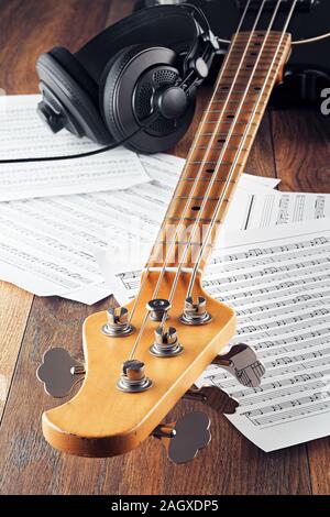 Chitarra basso collo, cuffie da studio e fogli di musica su un tavolo di legno. Concetto di musica la registrazione, la riproduzione o la composizione. Vista ravvicinata. Foto Stock