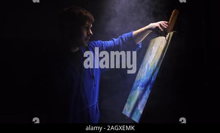 Artista copista paint seascape con nave in oceano. Fumo Vaper vape e-sigaretta. Artigiano arredatore disegnare come barca vela sul mare blu con colori acrilici. Foto Stock