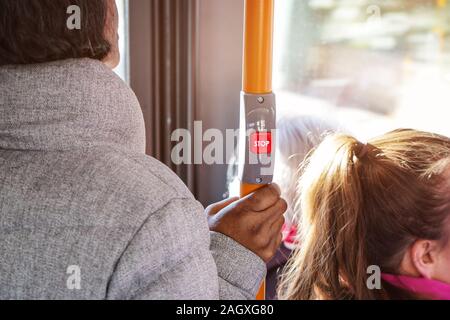 Anonimo donna pendolarismo sui mezzi di trasporto pubblico bus, dettaglio di sua mano tenendo la barra gialla sotto il pulsante stop, il sole che splende dietro lo sfondo della finestra. Foto Stock