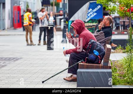 Montreal, Canada - Giugno, 2018: due senzatetto canadese uomini seduti sul banco di lavoro e il fumo di sigaretta. Foto Stock
