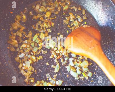 Cipolla fritti in padella con un cucchiaio di legno Foto Stock