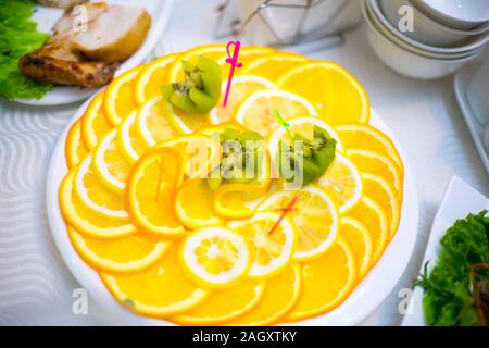 Pezzi tagliati a fettine di limone sono sparsi in un cerchio su una piastra e al di sopra di una fetta di kiwi. Snack al banchetto. Foto Stock