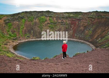 Veduta aerea astratta di una donna in giacca rossa che si erge ai margini del cratere vulcanico Kerid, Grimsnes, Islanda del Sud, cratere aereo lago estate Foto Stock