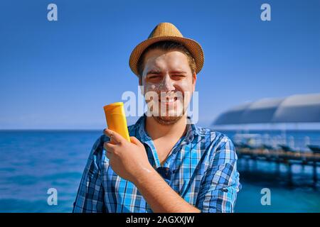 Guy mettendo in crema solare sulla faccia.L'uomo è in vacanza e ha cosparso con protezione solare e lo tiene in mano. Foto Stock