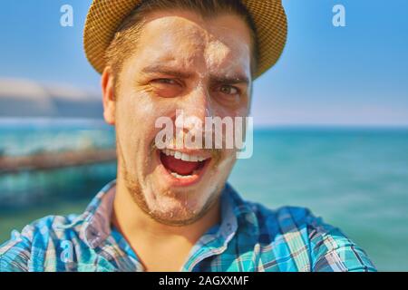 Guy mettendo su sun protection lozione sulla faccia.L'uomo è in vacanza e ha cosparso con protezione solare e lo tiene in mano. Foto Stock