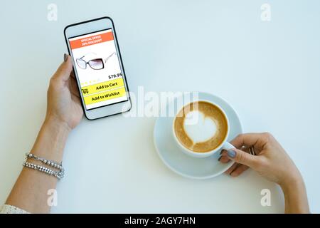 Panoramica delle mani di donne con lo smartphone lo shopping online pur avendo tazza di cappuccino in cafe Foto Stock