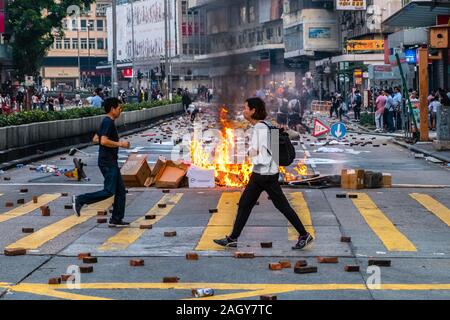 HongKong - Novembre 2019: la gente a piedi dalla strada bloccata e il fuoco che brucia sulla strada durante il 2019 HongKong proteste Foto Stock