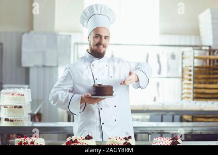 Pasticcere uomo sorridente holding torta sorridente in una pasticceria Foto Stock