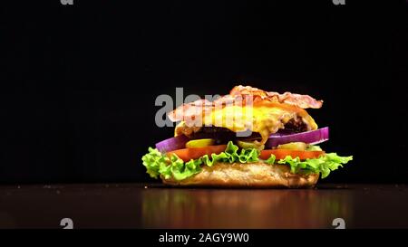 Craft burger di cottura è su sfondo nero. Sono costituiti da: salsa, lattuga, pomodoro, cipolla rossa, sottaceti, formaggi, pancetta, aria bun e in marmo la carne di manzo. Foto Stock