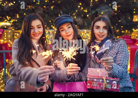 Anno nuovo concetto. Le donne amici burning botti in Leopoli da albero di Natale. Ragazze azienda borse per lo shopping e regali Foto Stock