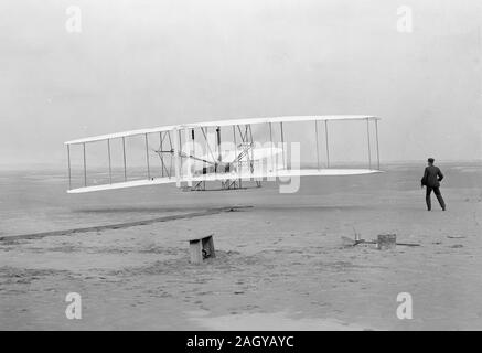 I fratelli Wright, il primo powered, controllata, un volo prolungato. Orville Wright ai comandi della macchina, che giace prono sulla aletta inferiore con fianchi in culla che gestiva l'ala-meccanismo di orditura. Wilbur Wright che costeggia per bilanciare la macchina, primo volo, 120 metri in 12 secondi, 10:35 del mattino; Kitty Hawk, North Carolina primo volo, Dicembre 17, 1903. Foto Stock