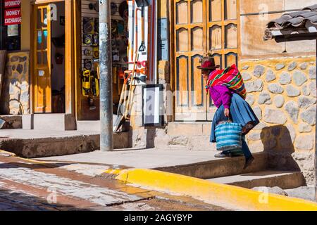 OLLANTAYTAMBO, Perù - Giugno 26, 2019: Donna Peruviana cholita vestito nel tradizionale tessuto colorato, porta sacchetti Foto Stock