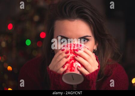 Donna che mantiene la Winter Cup con bel Natale motivo chiudere fino a Natale sfondo. Inverno e tempo di Natale concetto. Foto Stock