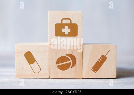 Close up di cubi con icone mediche del medico del sacco, pillole, siringa su sfondo di legno. Concetto di kit di primo soccorso. Foto Stock