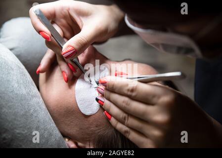 Mazzetto di ciglia artificiali in pinzette. Estensioni delle ciglia artificiali, processo chiudere la donna in un salone di bellezza. La bellezza e la cura di sé. Foto Stock