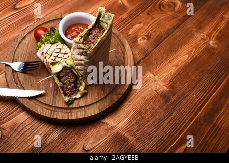 Flatbread con carne di maiale o di pollo ripieno e il peperoncino rosso salsa. La carne macinata avvolto con pane lavash su sfondo di legno. Il fast food concept. Burrito o tortilla è servita nel ristorante o bar. Foto Stock