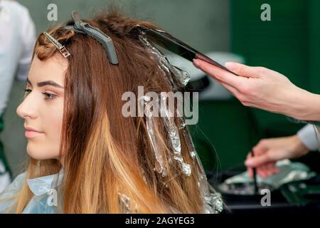 Giovane donna la ricezione di tingere i capelli dal parrucchiere al salone di parrucchiere. Foto Stock