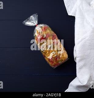 Trasparente sacchetto cellophane con materie colorate di pasta a forma di prua su un blu superficie in legno, spazio di copia Foto Stock