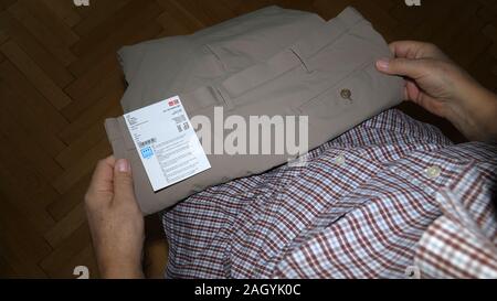 Parigi, Francia - Sep 13, 2019: POV vista aerea del senior uomo unboxing spacchettamento confezione di plastica da Uniqlo fashion brand con più coppie di eleganti pantaloni a misurare la dimensione Foto Stock