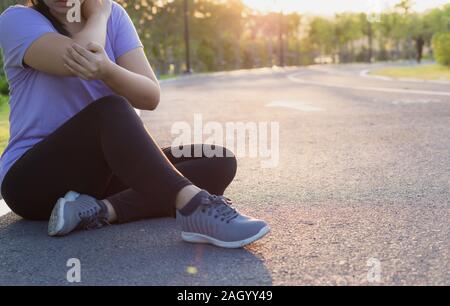 Un atleta femminile soffre di braccio e il gomito dolore e ferite al parco. Lo sport e il concetto di assistenza sanitaria. Foto Stock