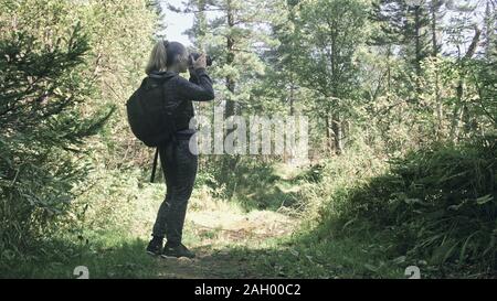 Traveler fotografare la vista panoramica nella foresta. Una donna caucasica bello scatto magic look. Ragazza scatta foto video su mirrorless reflex fotocamera. Foto Stock