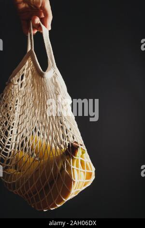 Mano trattiene un eco borsa a rete con ramo di banana su sfondo nero. Foto Stock