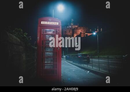 Edimburgo, Scozia, 13 dicembre 2018: il vecchio Britannico rosso phone booth di fianco alla strada di notte con castello in background. Foto Stock